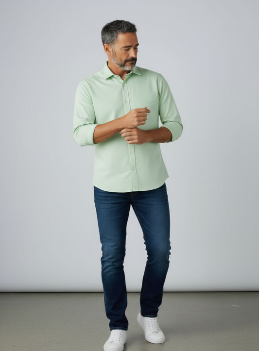 Man wearing a light green shirt and blue jeans against a plain background