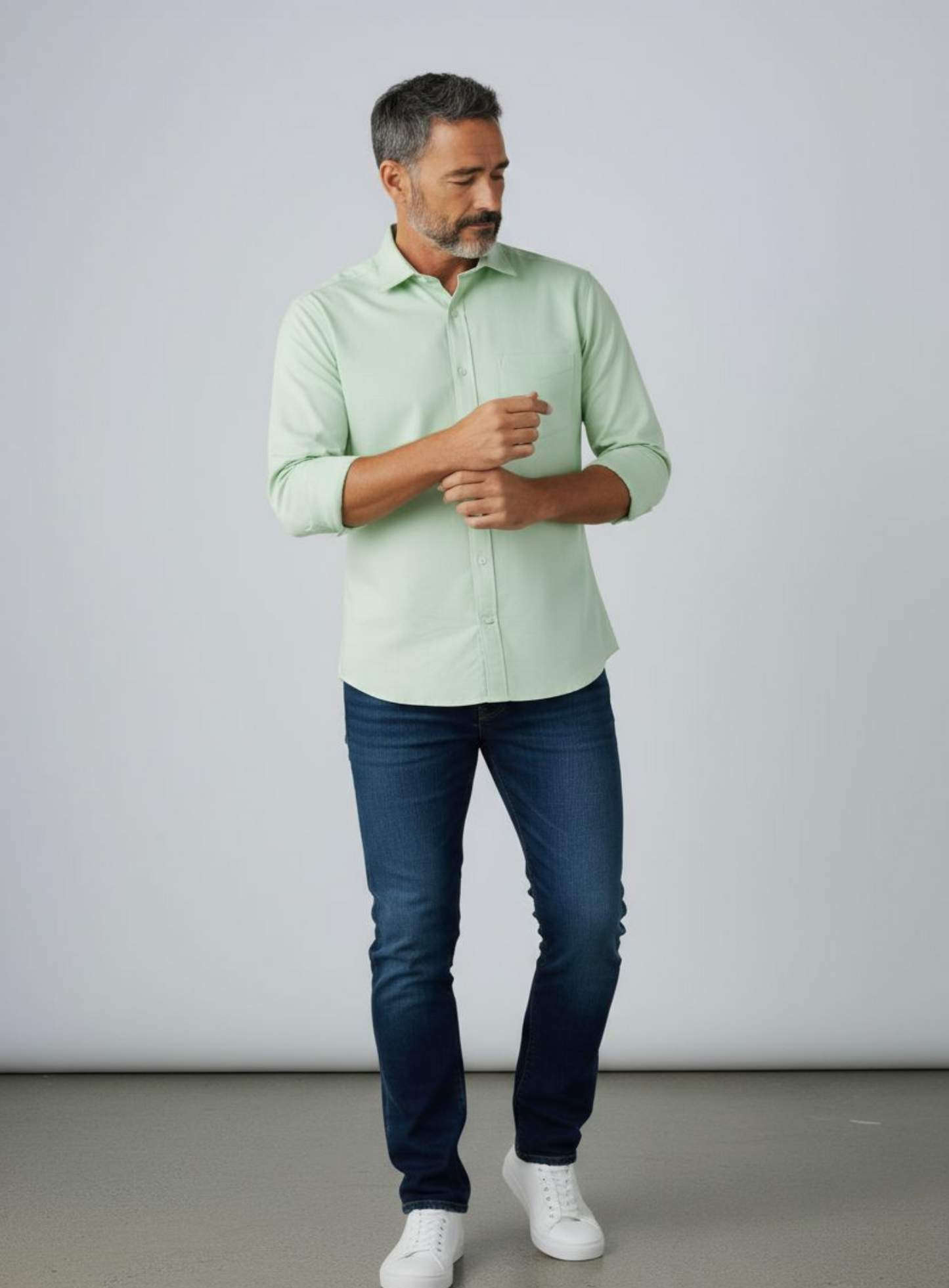 Man wearing a light green shirt and blue jeans against a plain background