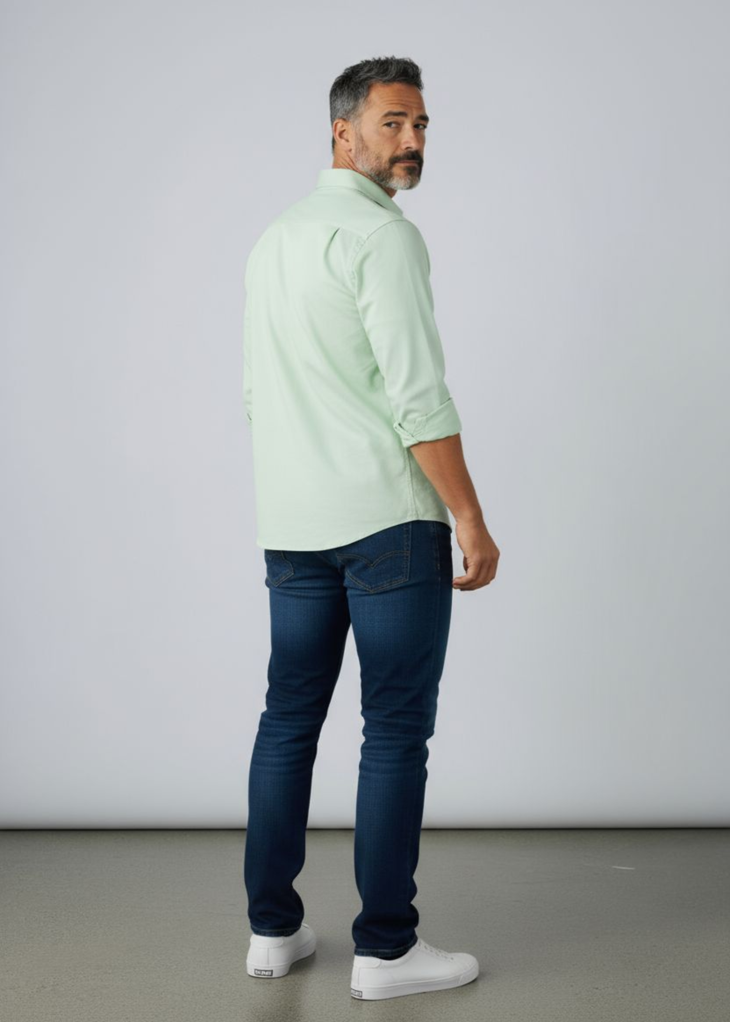 A man wearing a sage green colour shirt with a dark blue jean and a pair of sneaker 