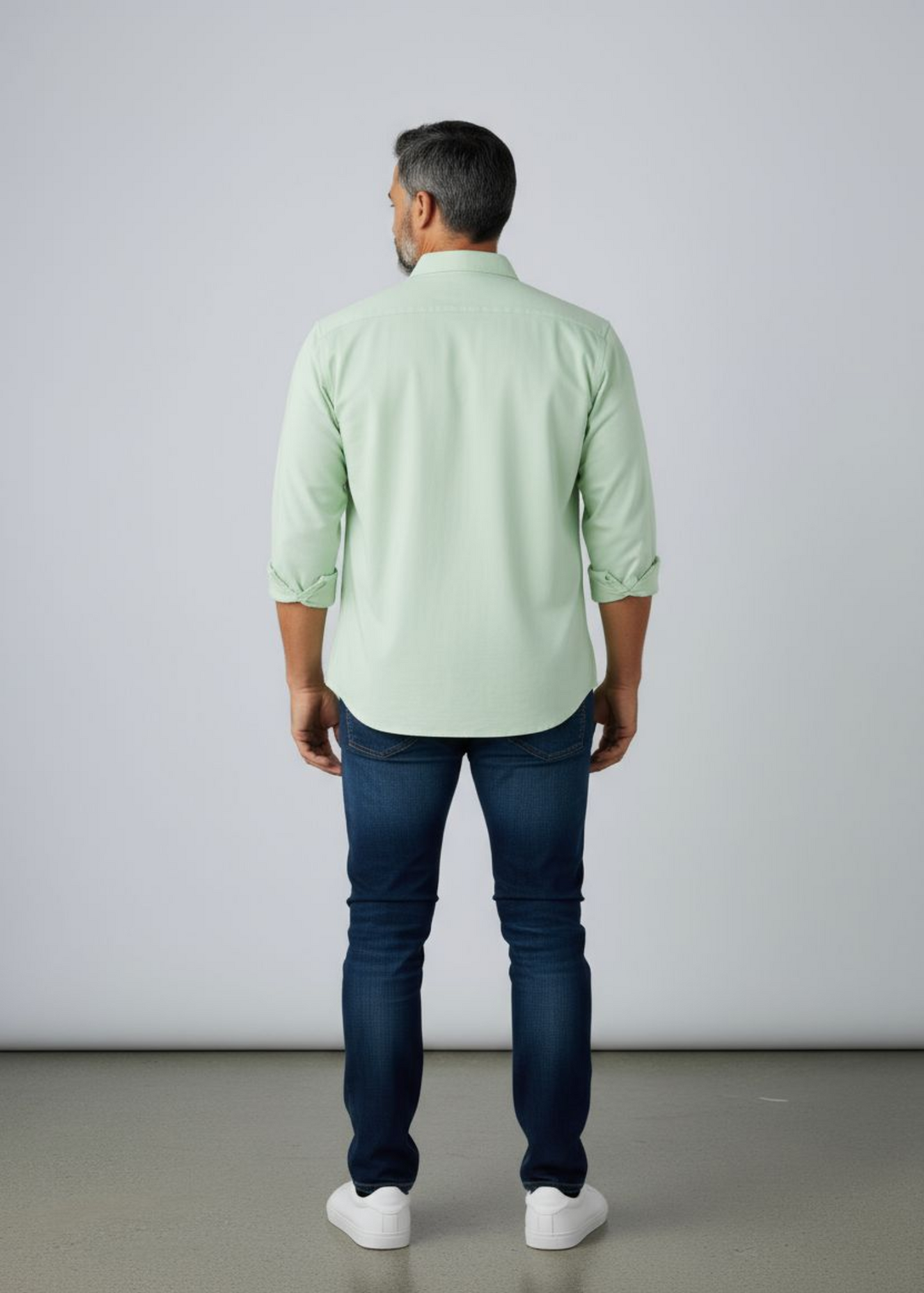 A man wearing a sage green colour shirt with his back showing and a dark blue jeans in a causa wear setting